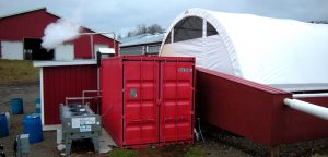 The equipment and controls, as well as the engine, are housed in a shipping container (foreground) that is adjacent to the solids separator building (right). 