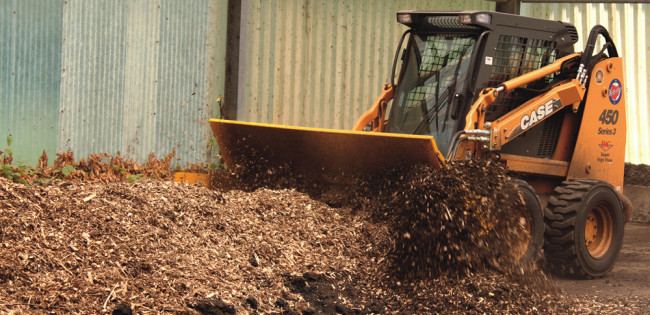 A row of new wood chips is put down, then topped with layers of finished compost and biosolids. Feedstocks are mixed with a Brown Bear aerator attached to a skid loader.