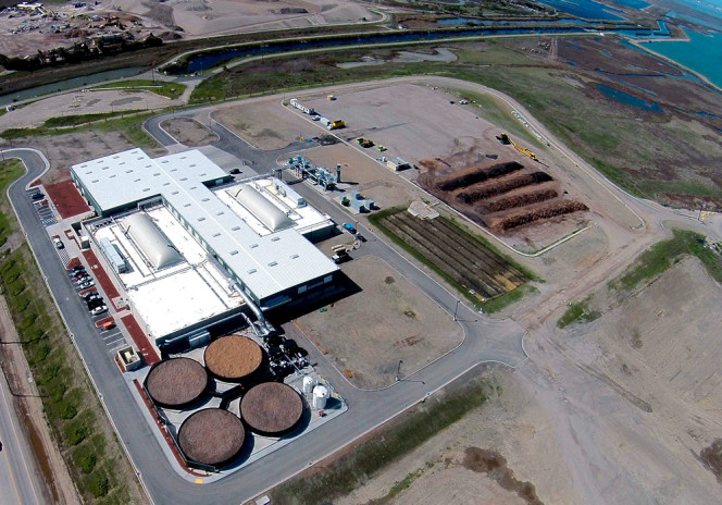 Aerial photo highlights the processing building, biogas storage bladders (on left and right on roofs in center of photo) and the four circular biofilters (bottom of photo) treating building air. The outdoor windrow composting curing pad is on far right.
