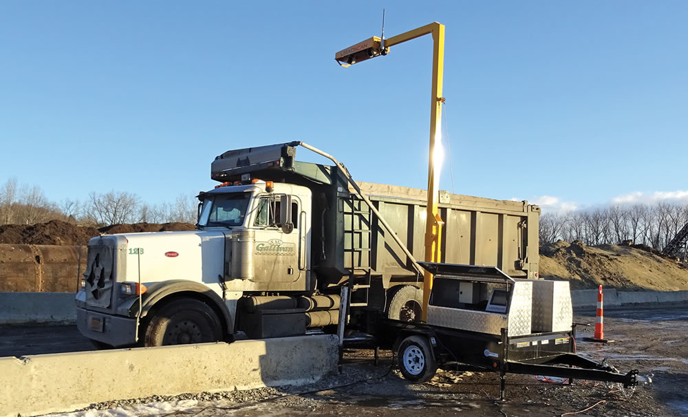 An open-top truck containing materials passes under a load volume scanner, which maps a 3-D image of the load.