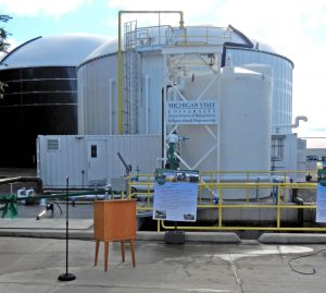 The feedstock receiving area (foreground) includes an open- air receiving pit for “low energy” feedstocks like manures, and a covered receiving area for “high energy” feedstocks like food scraps and FOG.