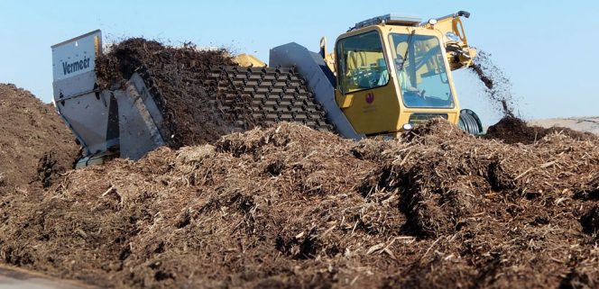 An aerated mass bed system is used for composting yard trimmings, and eventually food waste. An elevating face turner moves material 22 feet laterally on the pad in each turning event. Aeration piping is housed in a gravel bed below the concrete slab with nozzles flush with the slab surface. The aeration system can be run in all positive, all negative, or in a reversing positive-negative loop. P